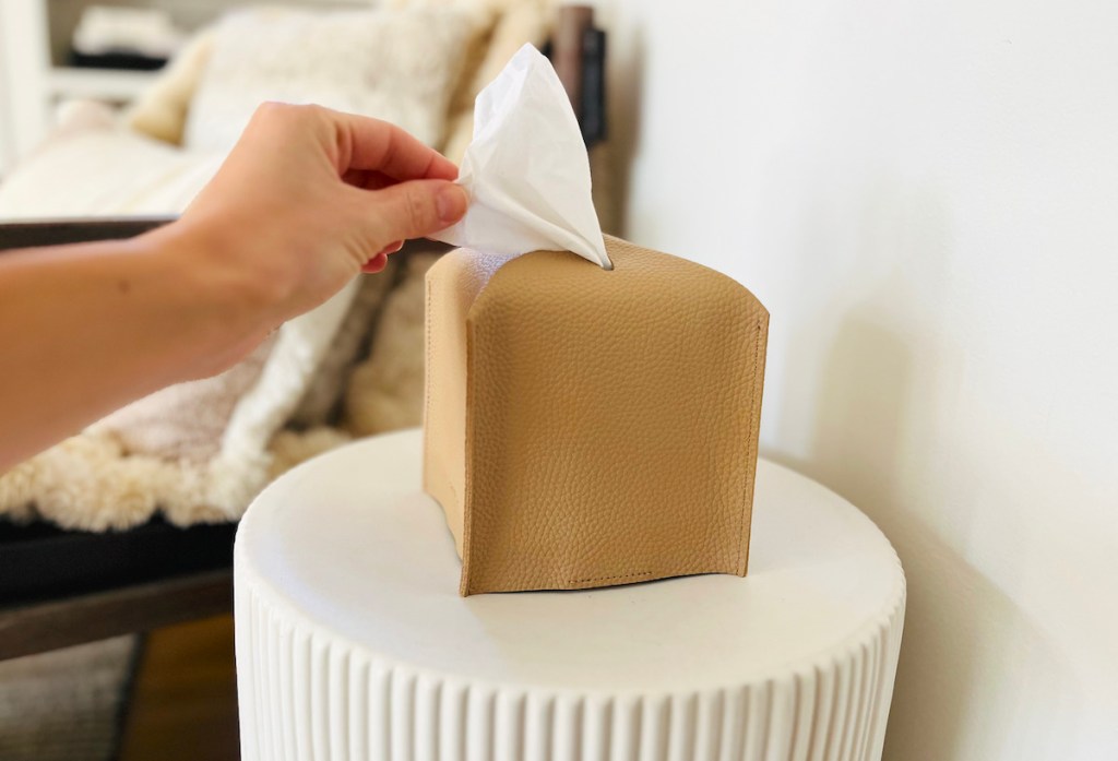 hand pulling tissue out of leather covered box on white side table