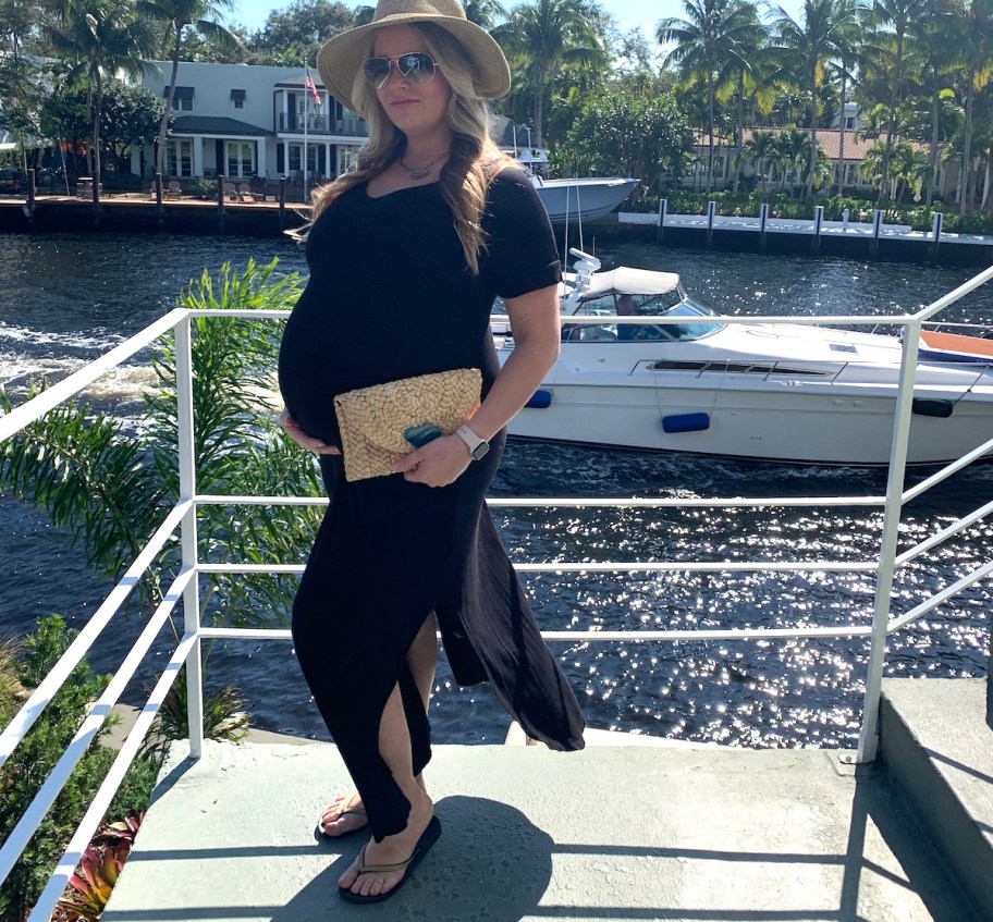 woman holding belly wearing black maxi dress at marina