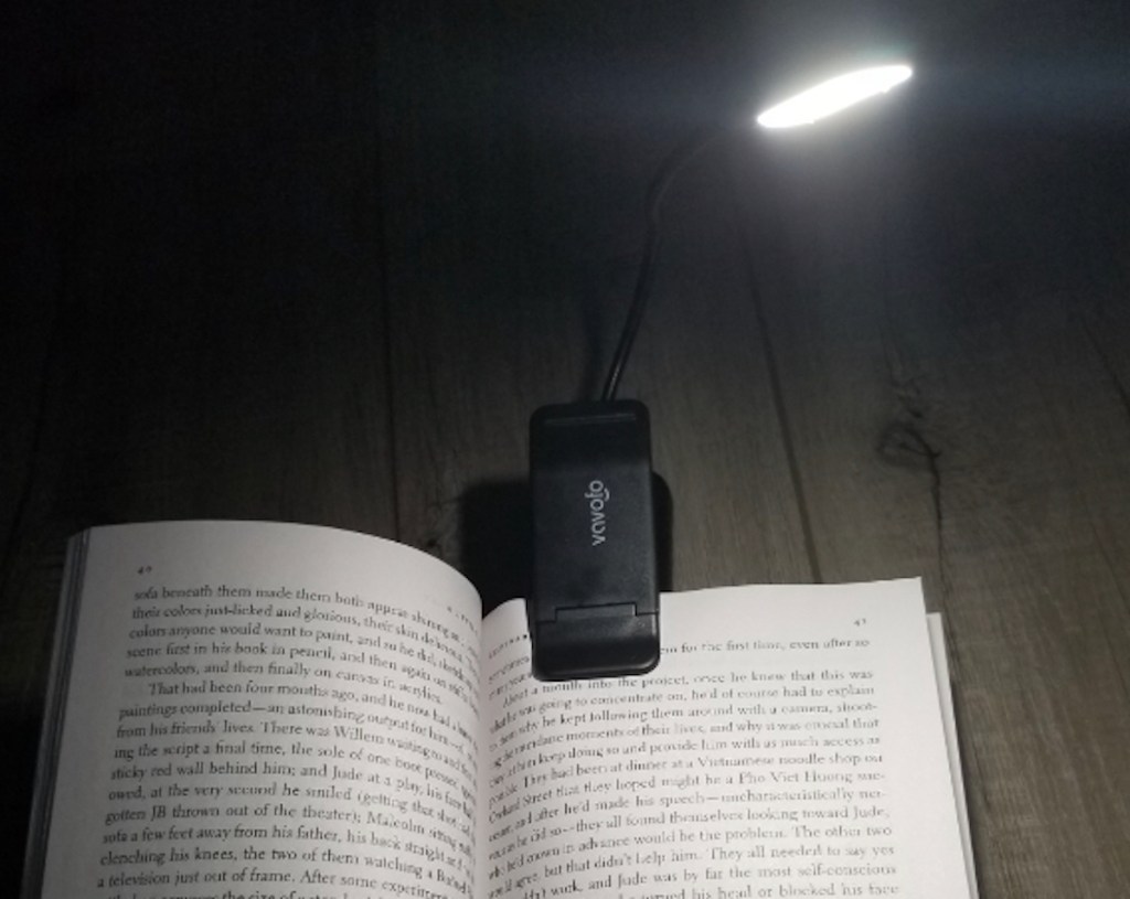 open book with black clip on light on top of pages