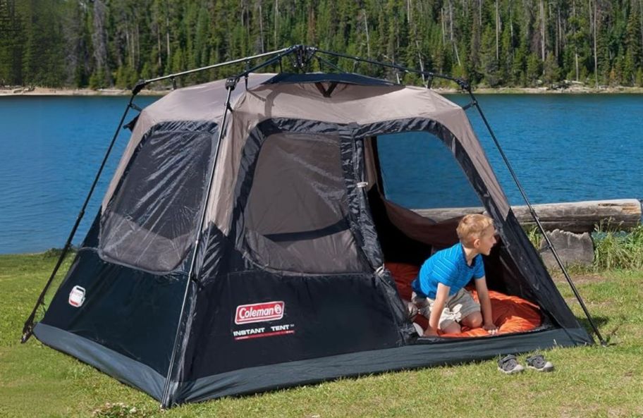 a little boy leaning out the door of a tent set up next to a lake