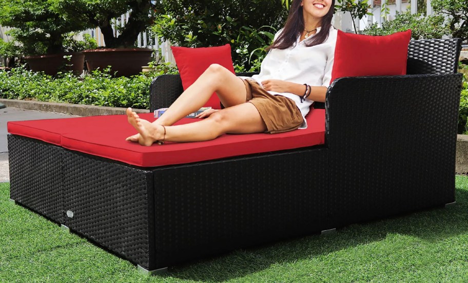 woman sitting on red rattan daybed in grass