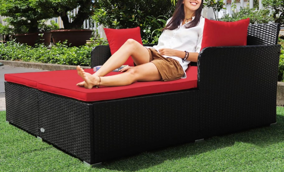 woman sitting on red rattan daybed in grass