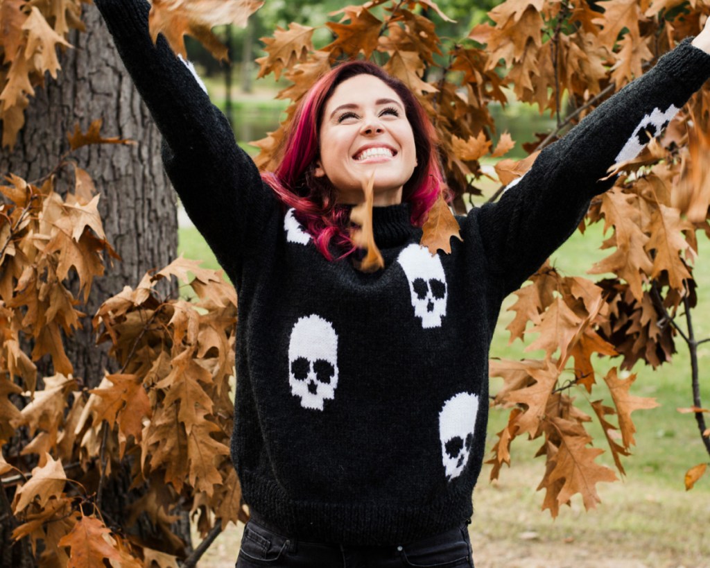 woman throwing up leaves in skull sweater