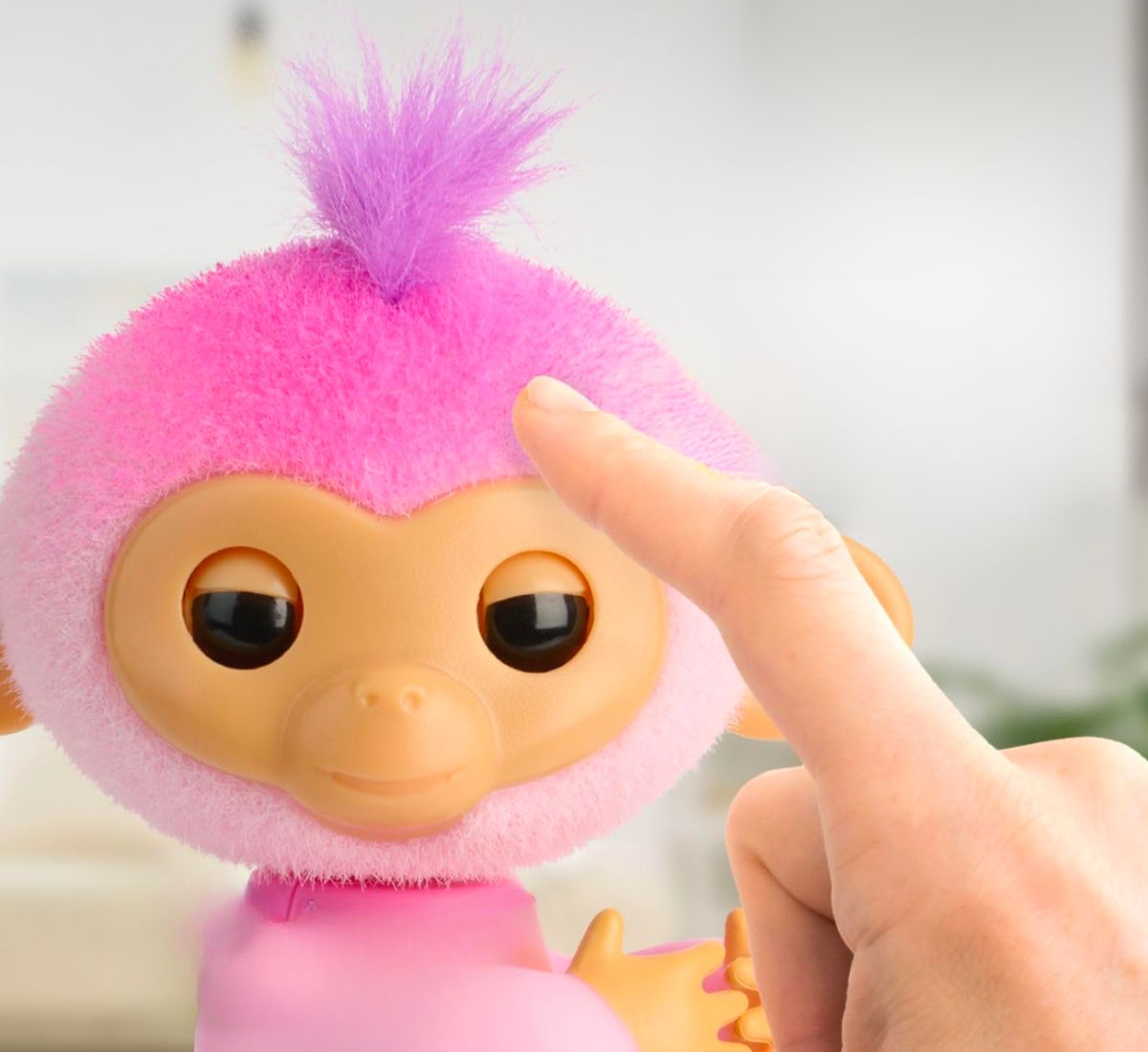 a finger reaching out to pet a pink fingerlings monkey named harmony with fuzzy hair on her head