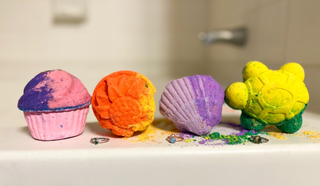 four colorful bath bombs and rings on side of tub