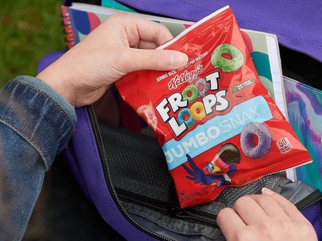 a hand putting a pack of kellogg's froot loop jumbo snax into a backpack