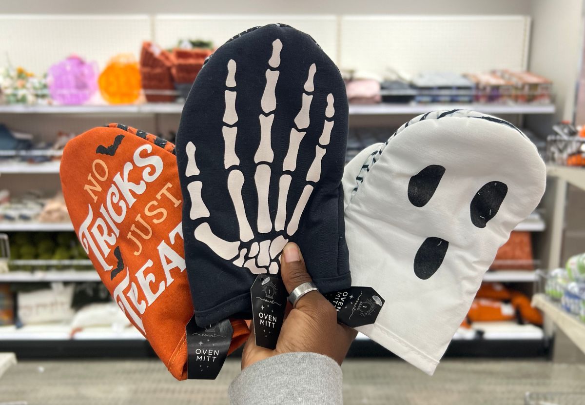 a womans hand holding up three assorted halloween oven mitts
