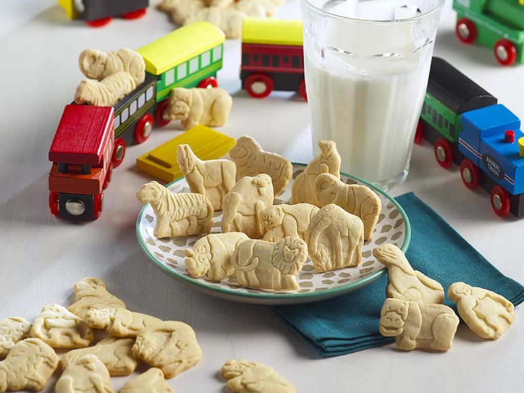 a variety of happy belly animal cookies on a plate with a glass of milk and toy trains in the background