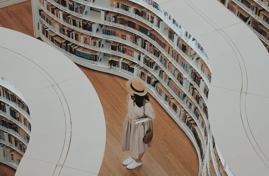 woman standing in library aisle with tons of books on wavy white shelves