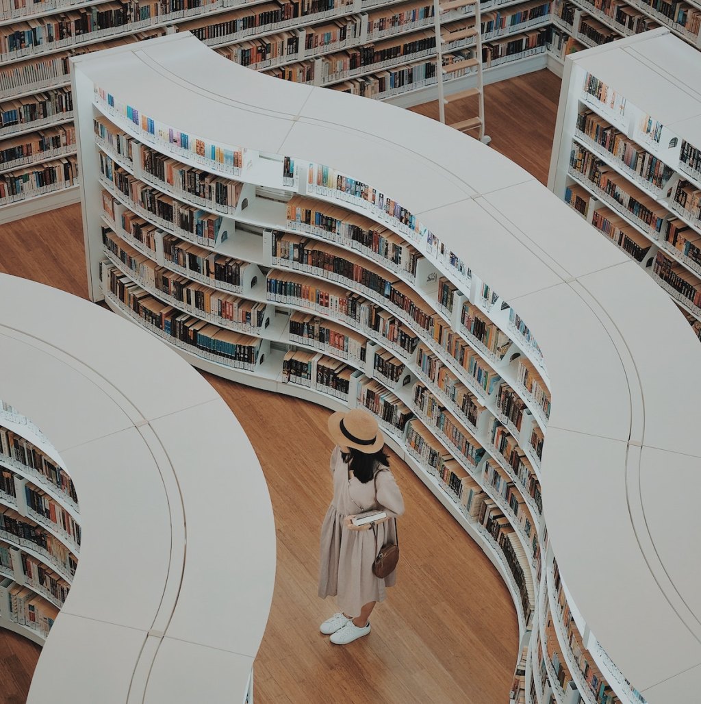 woman with a hat standing in library with curvy aisles of books
