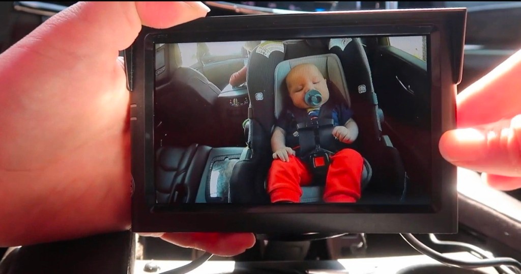hands holding baby camera with image of baby in carseat