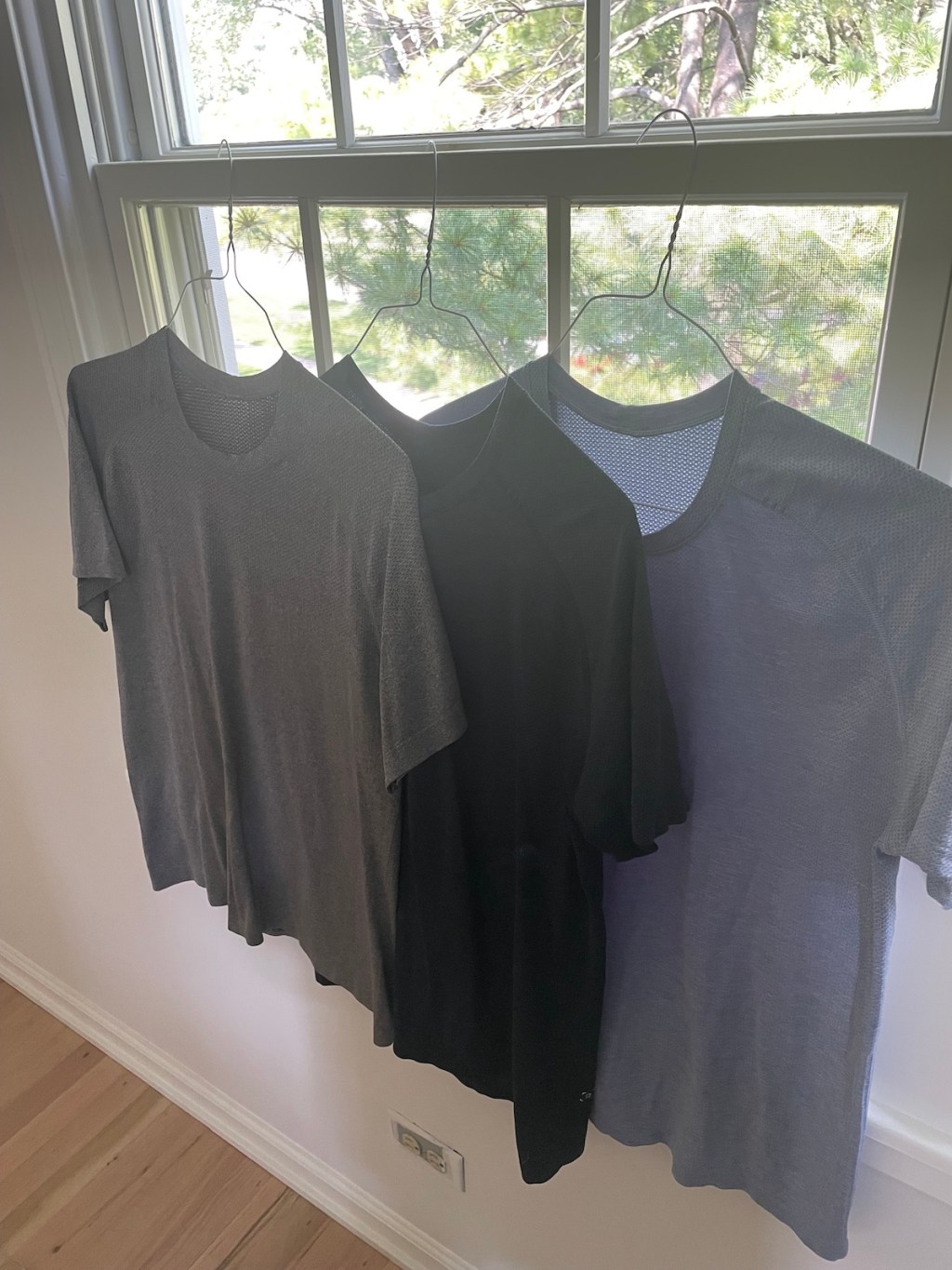 black and gray lululemon tshirts hanging from window on wire hangers