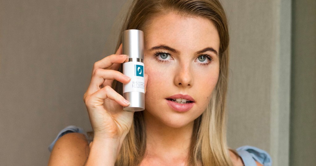 woman holding osmotics blue copper eye cream next to her face