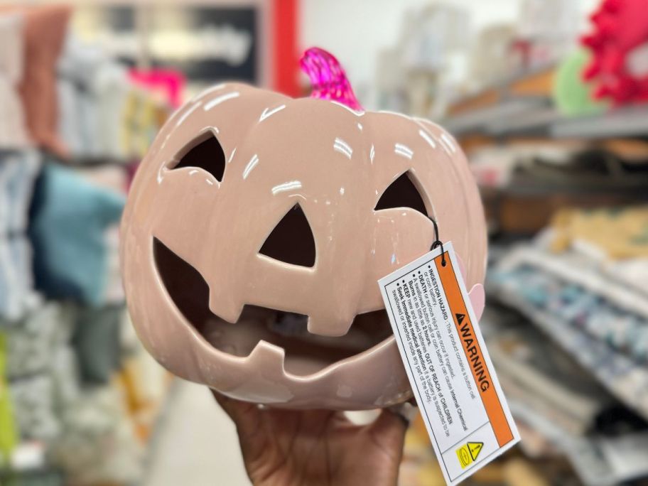 pink ceramic pumpkin being held by hand in store aisle