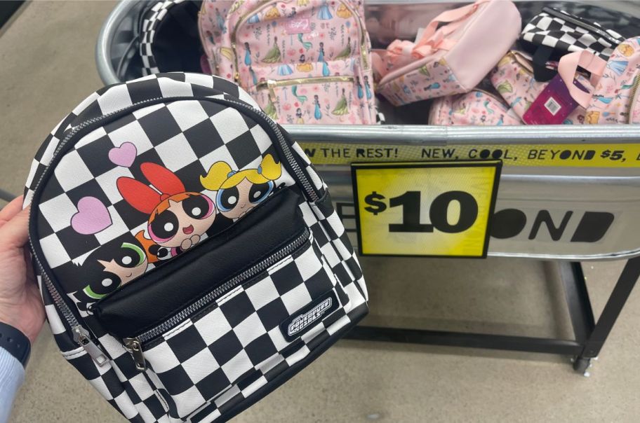 a womans hand holding a Powerpuff girls mini backpack with a disney princess mini backpack in background