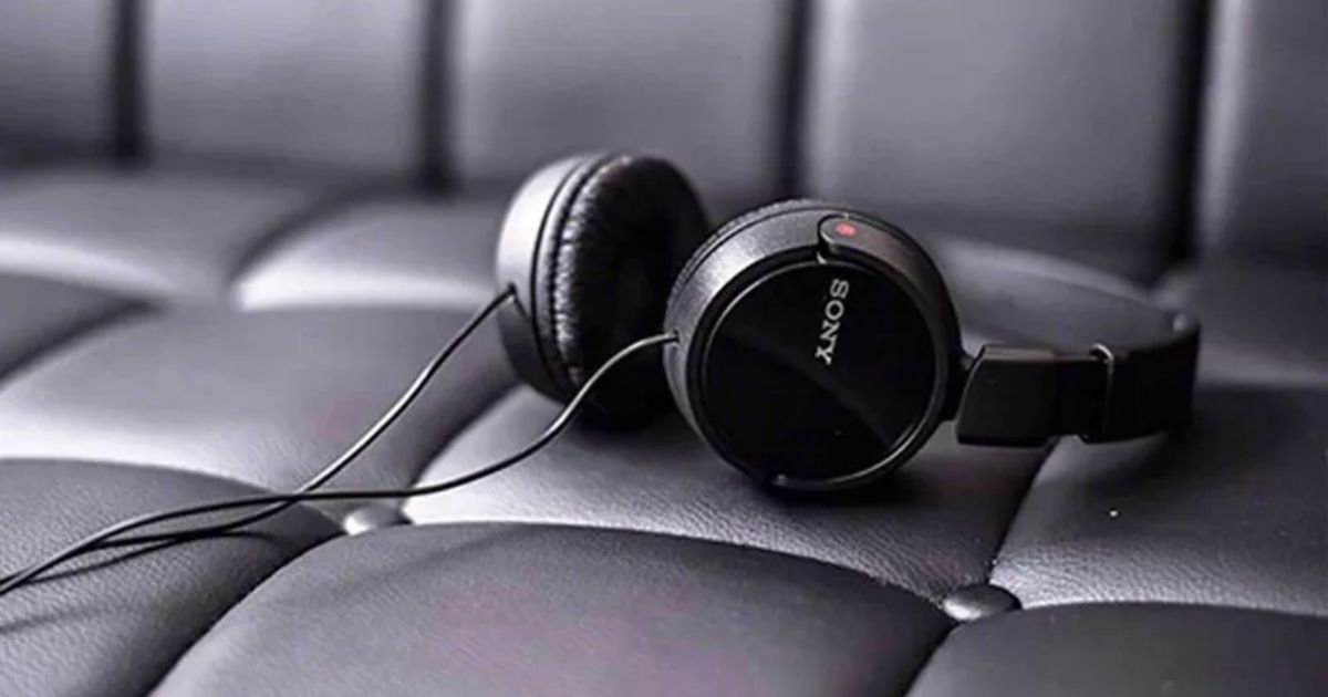 a pair of black sony wired headphones laying on a black leather sofa
