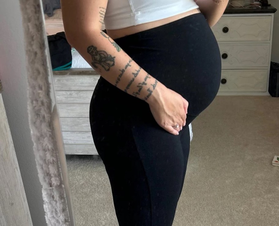 woman holding belly in mirror wearing black leggings