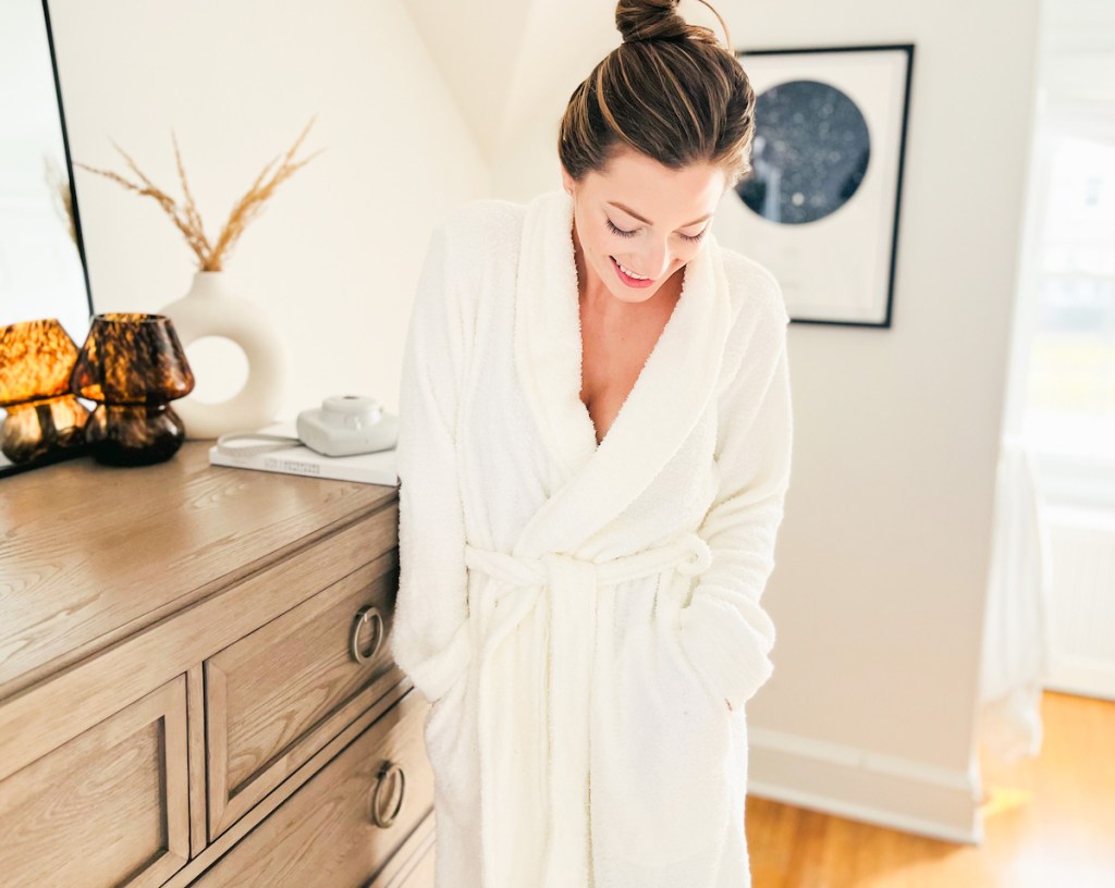 woman looking down at white robe standing in bedroom