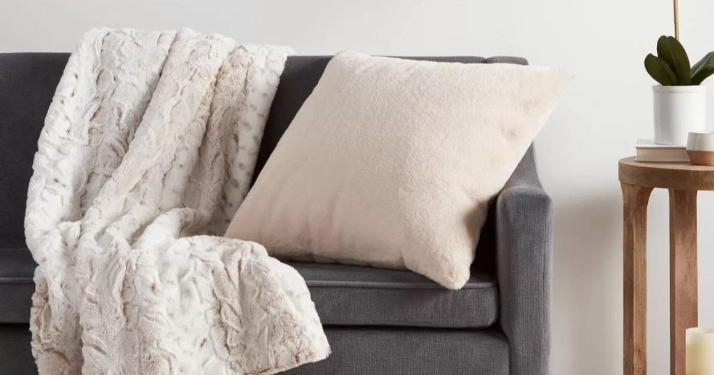 cream colored faux fur square pillow on gray couch next to white blanket