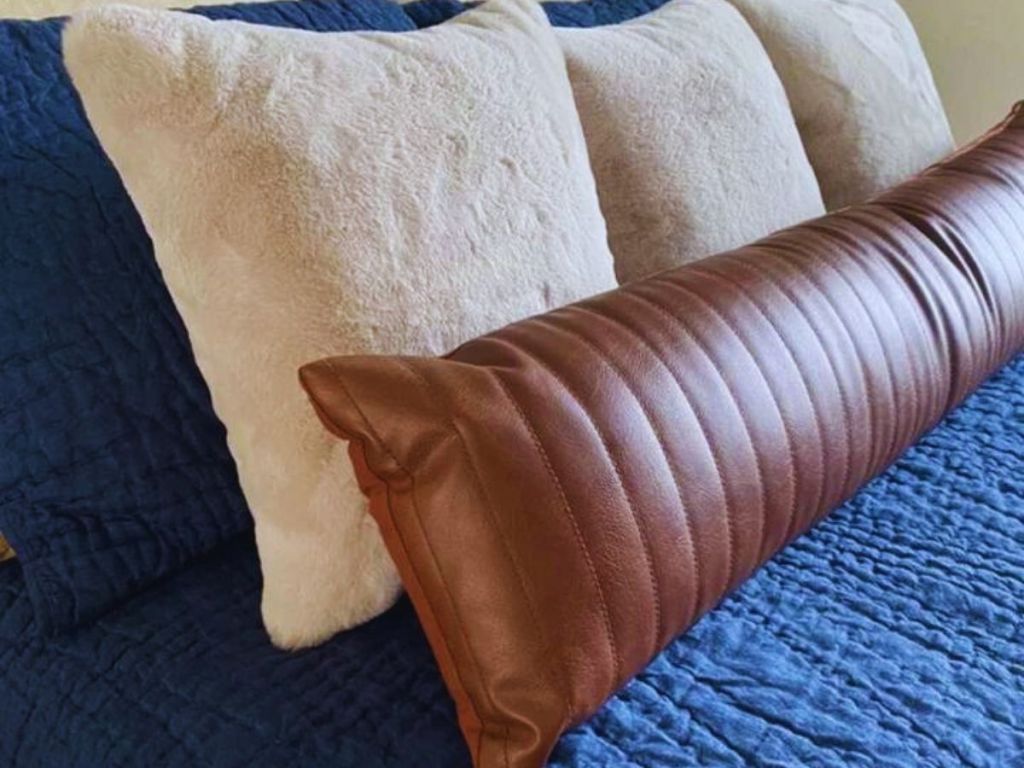 3 cream square pillows behind brown leather pillow on blue bedding
