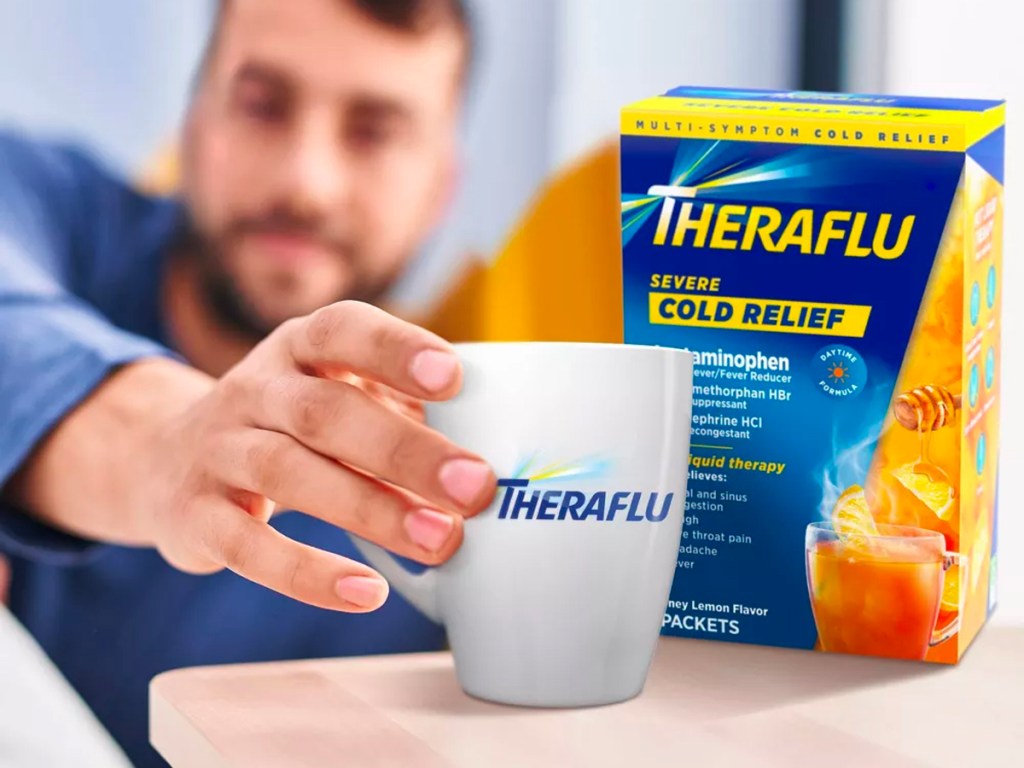 man reaching for coffee mug next to box of theraflu medicine