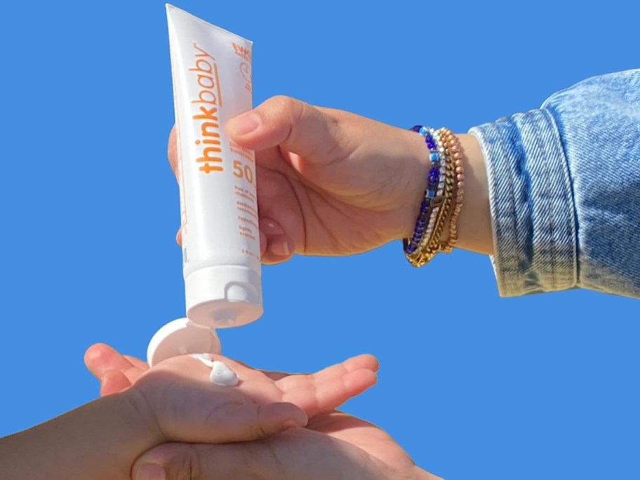 woman squeexing thinkbaby sunscreen into a small child's hand