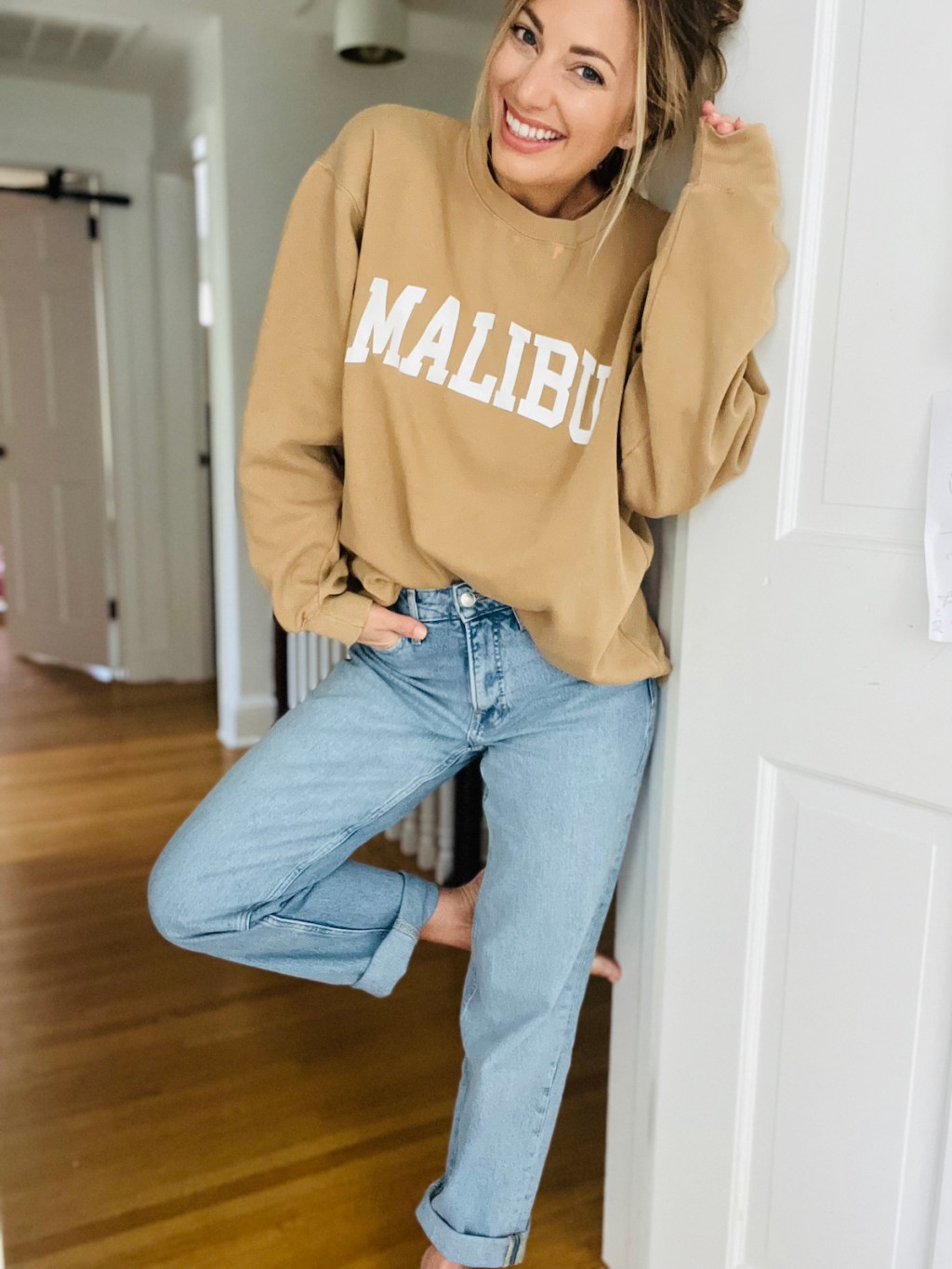 woman standing in doorway wearing loose jeans and malibu sweatshirt