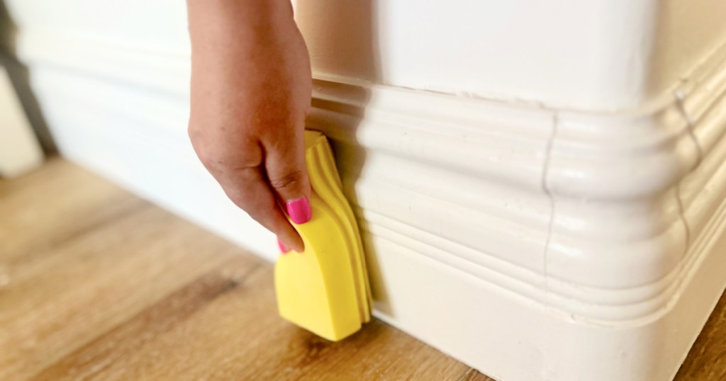 woman cleaning baseboards with a damp duster sponge