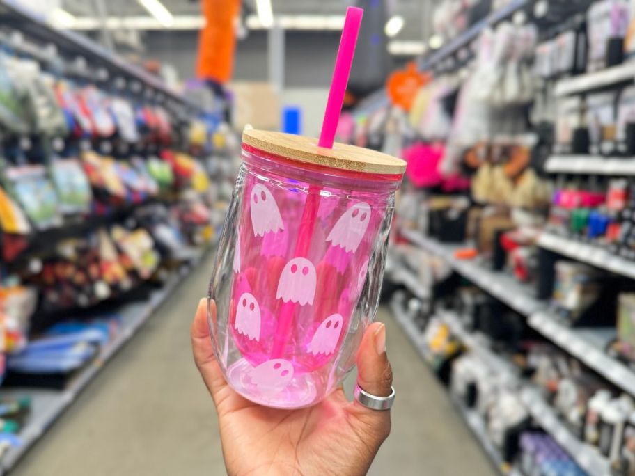 hand holding a pink glass tumbler with wood top that has ghosts on it