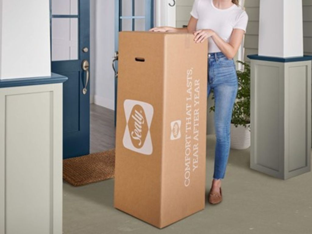 Woman on front porch standing next to a Sealy Memory Foam Mattress Box