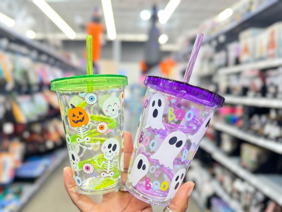 hand holding plastic Halloween tumblers with lids and swirly straws