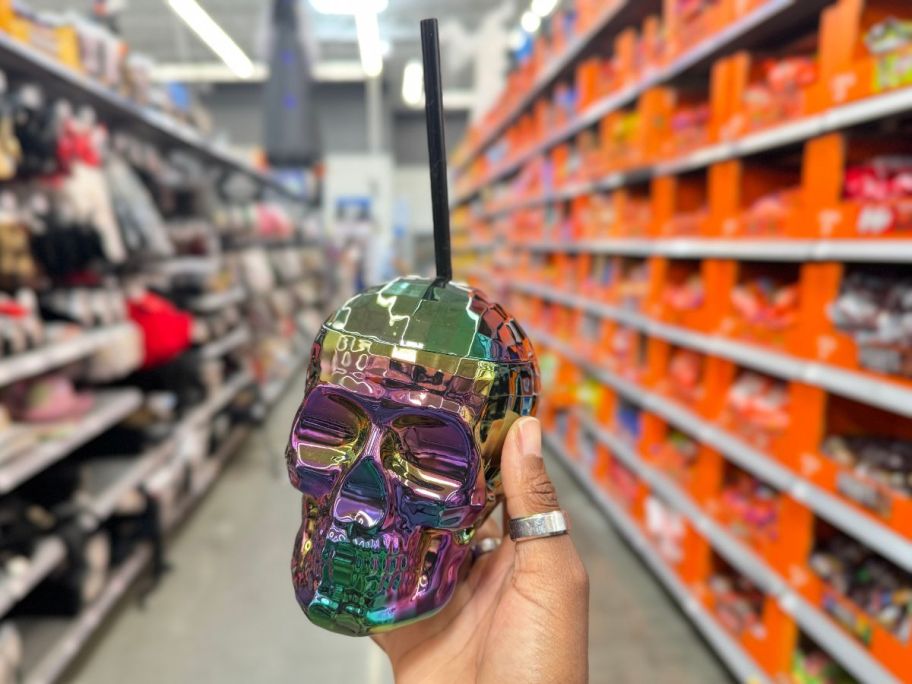 hand holding a black and iridescent skull shaped Halloween cup with a straw