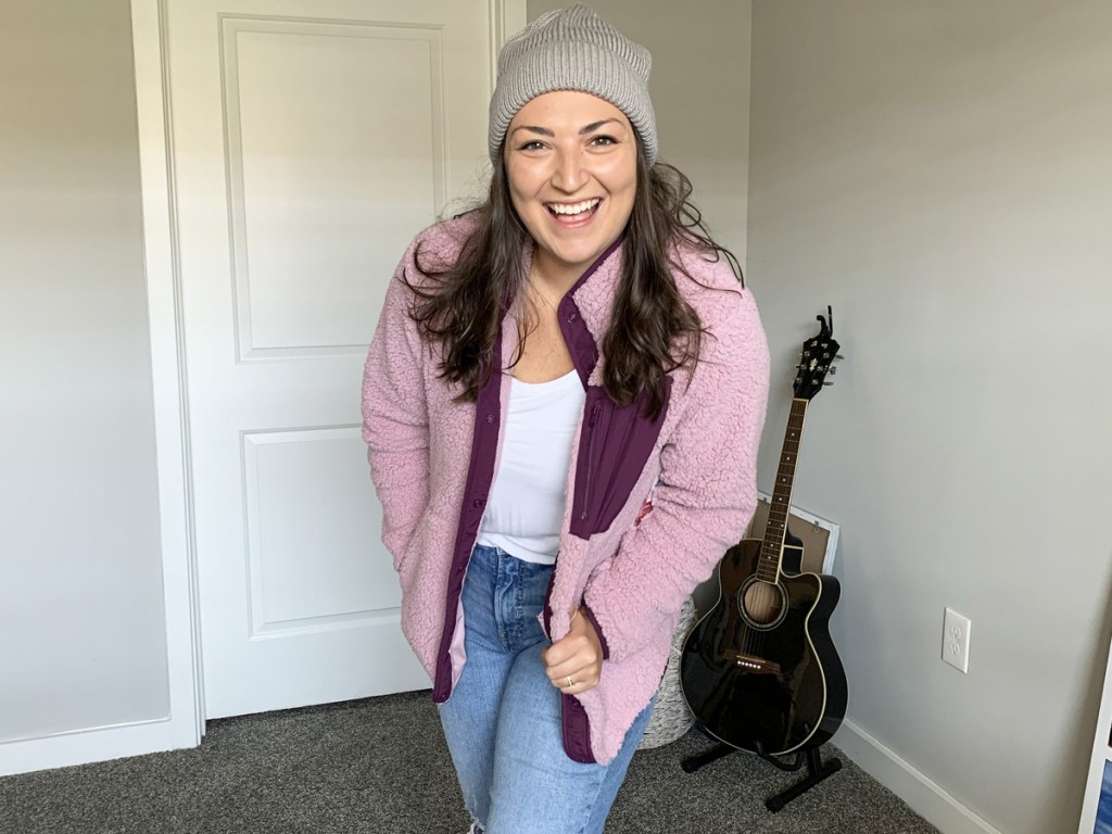 woman wearing a pink sherpa jacket, white top, jeans, and grey beanie