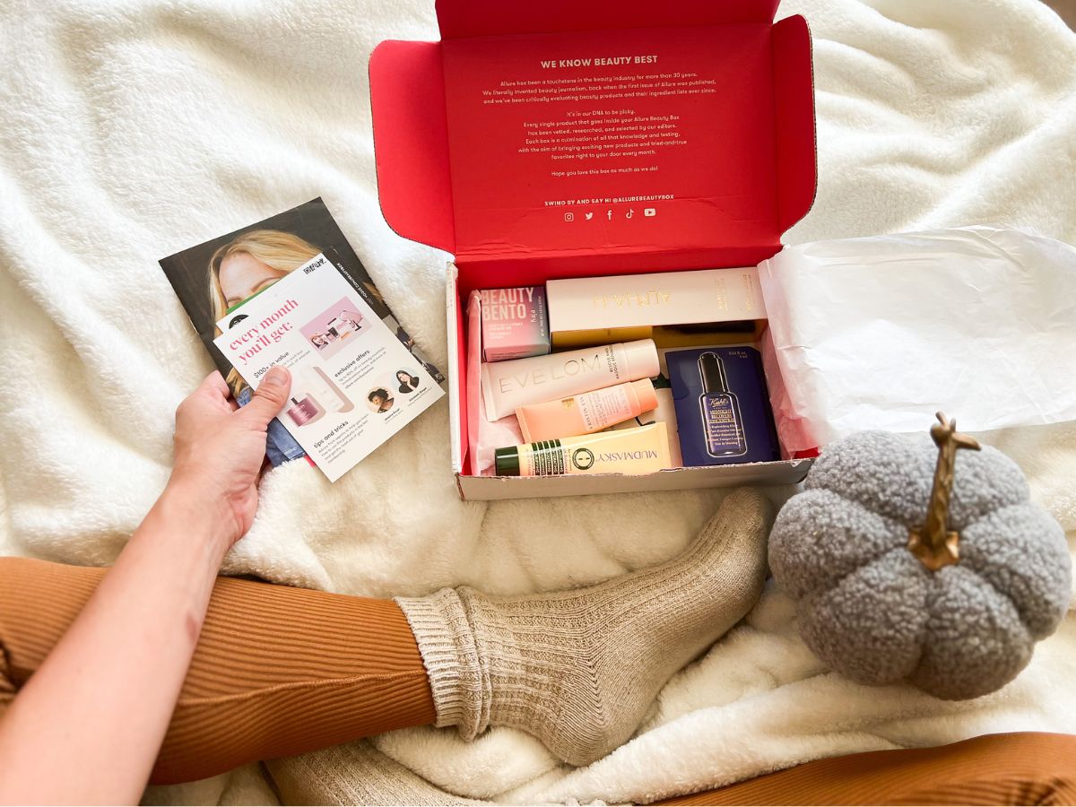Woman sitting on a bed with an open Allure Beauty Box set in front of her