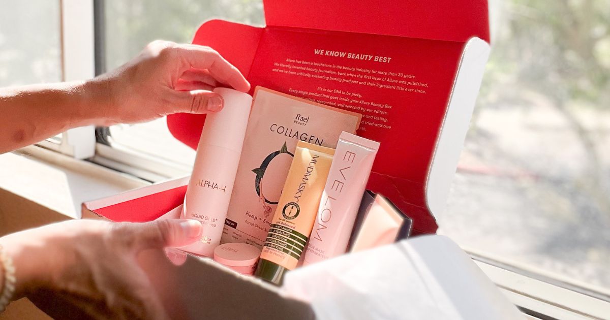 Allure's September 2023 Beauty Box sitting on a windowsill with the contents exposed with a hand touching one of the full-size products