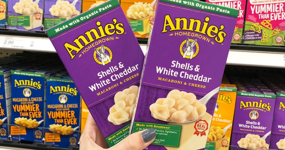 hand holding up two purple boxes of Annie’s White Cheddar Shells Macaroni & Cheese