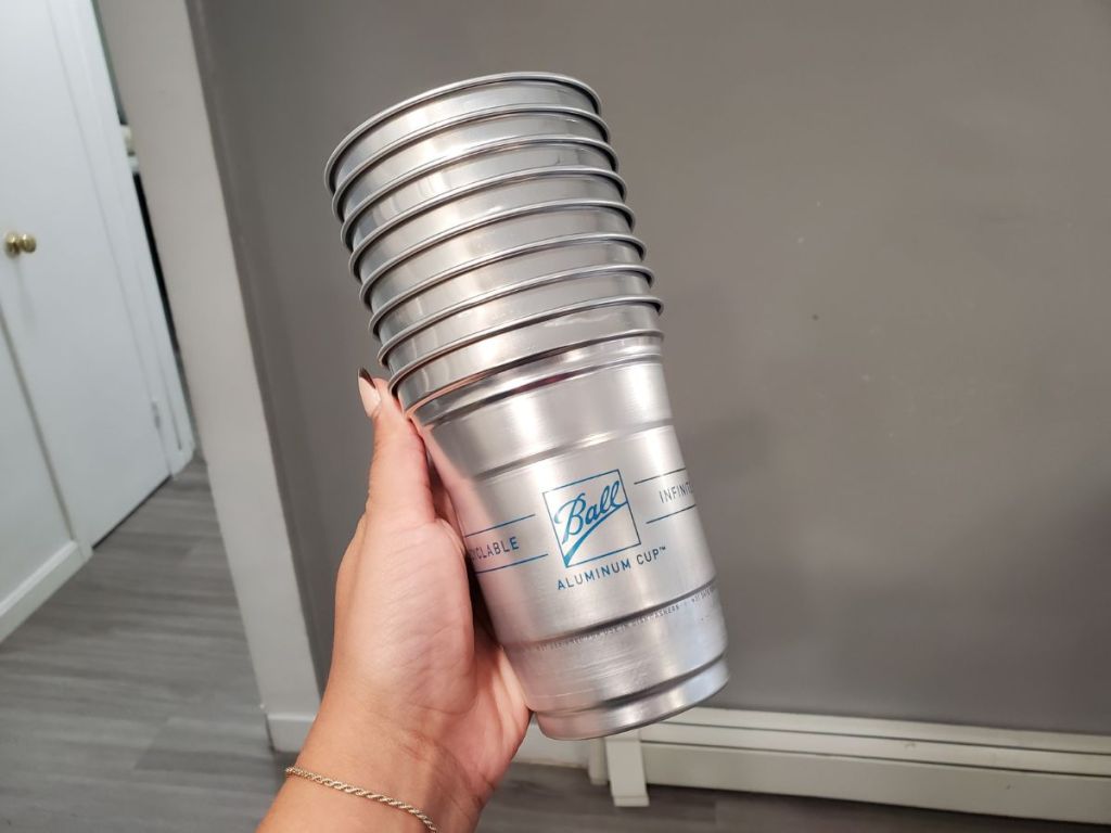 A hand holding a stack of Ball Reusable Cups