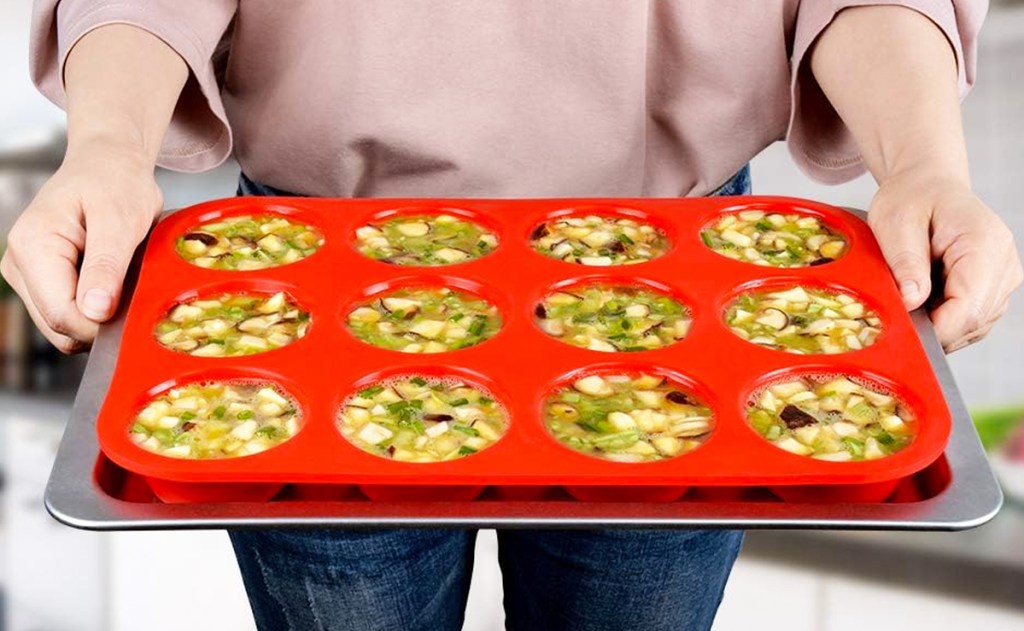 woman holding a tray with a red silicone muffin pan
