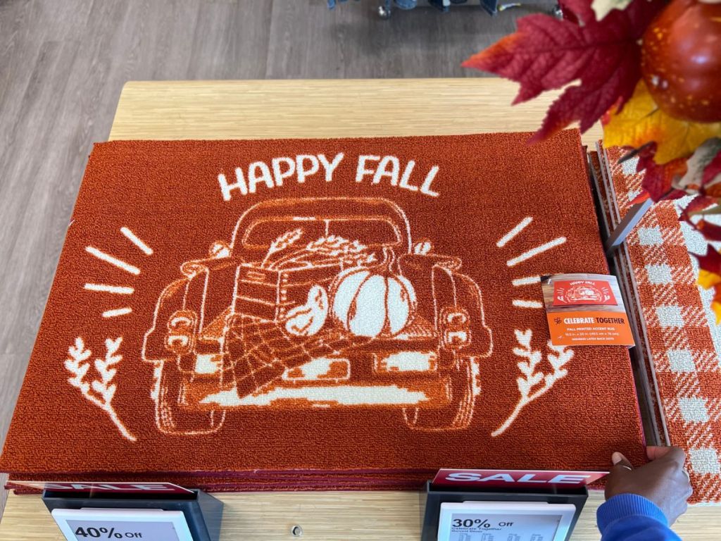 A hand holding a Celebrate Together Fall Happy Fall Harvest Accent Doormat