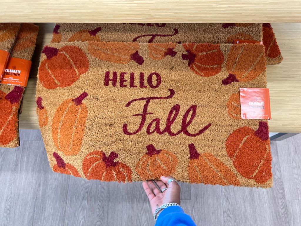 A hand holding a Celebrate Together Fall Happy Fall Harvest Accent Doormat