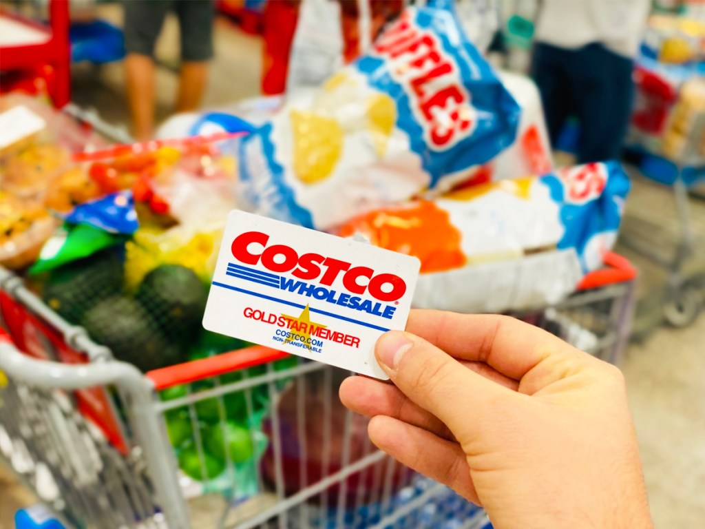 hand holding a costco membership card in front of shopping cart