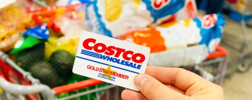 hand holding a costco membership card in front of shopping cart