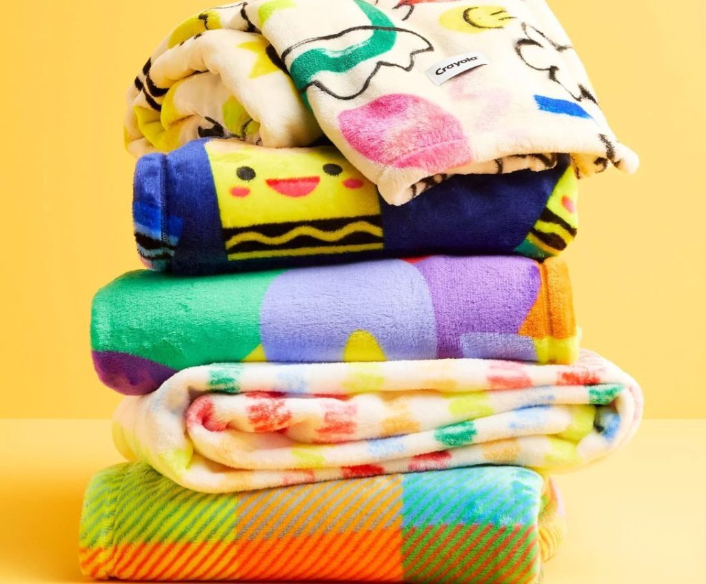 A stack of plush throw blankets from the Crayola X Kohl's Collection
