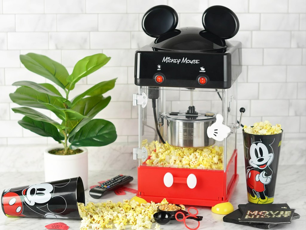 mickey mouse popcorn maker, cups, and measuring scoops with popcorn around them