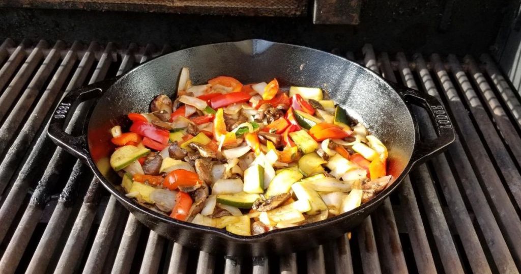Lodge 8" Cast Iron Skillet on a grill with meat and veggies cooking in it
