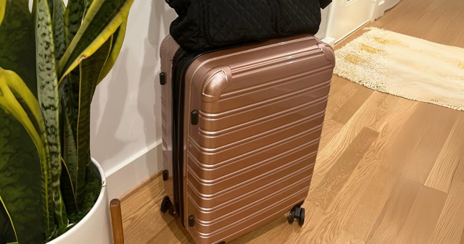 rose gold iFLY hardside suitcase with a duffel bag on top sitting by a door