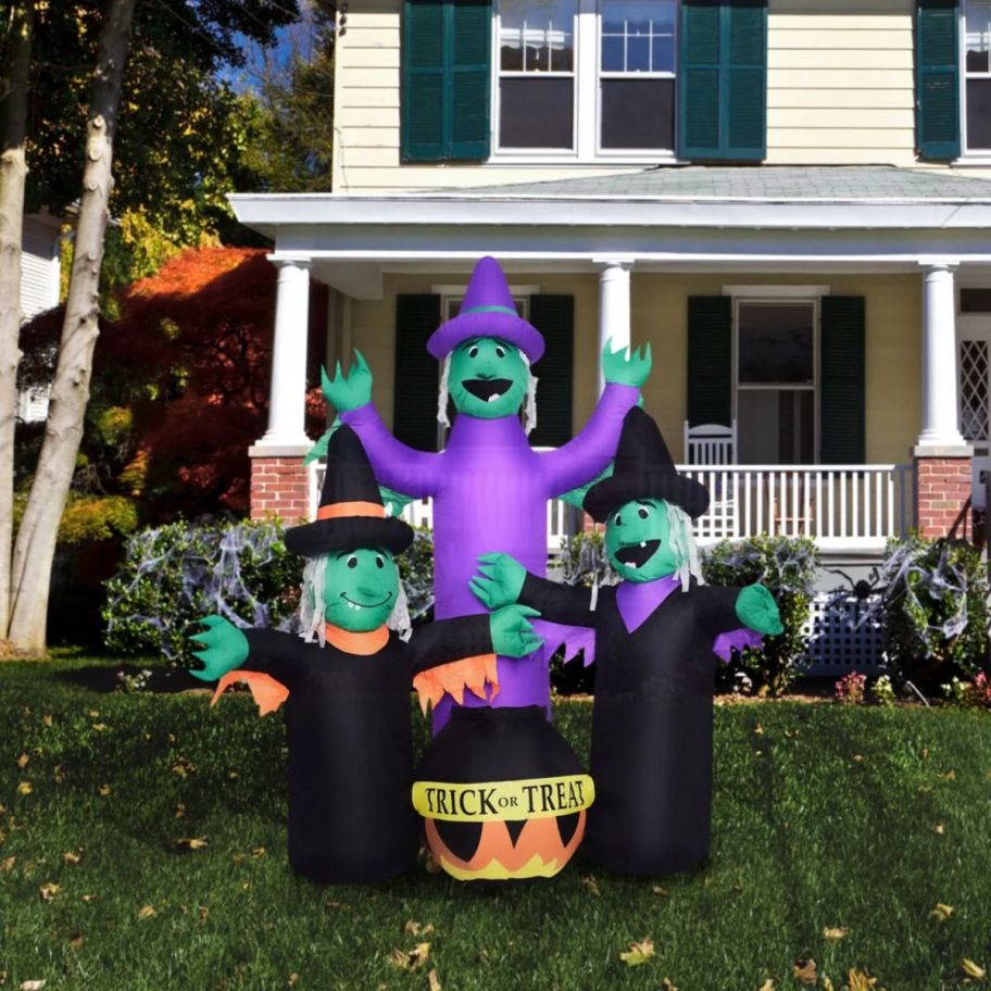 Inflatable witch trio with a cauldron in front of a house.