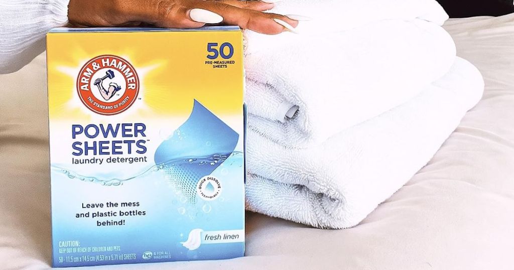 Arm & Hammer Power Sheets Laundry Detergent, Fresh Linen 50ct sitting beside folded towels with woman's hand on top