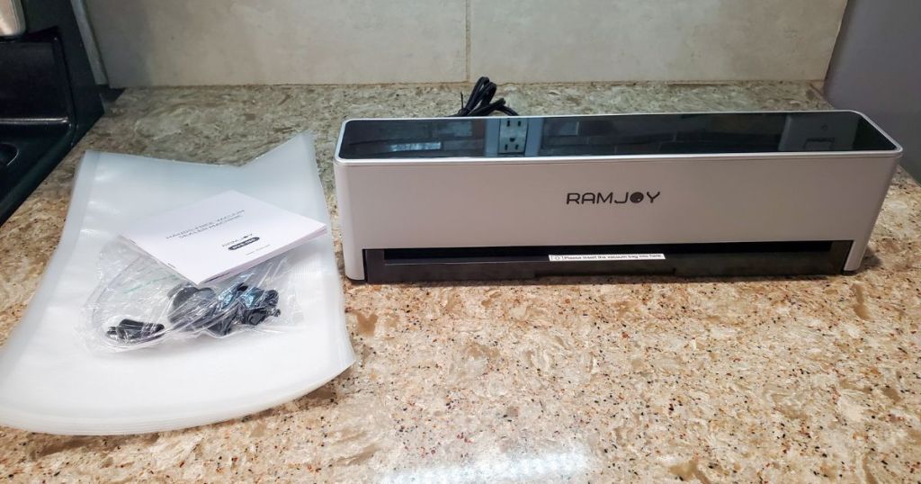 RAMJOY Hands Free Vacuum Food Sealer with bags and instructions sitting on a counter