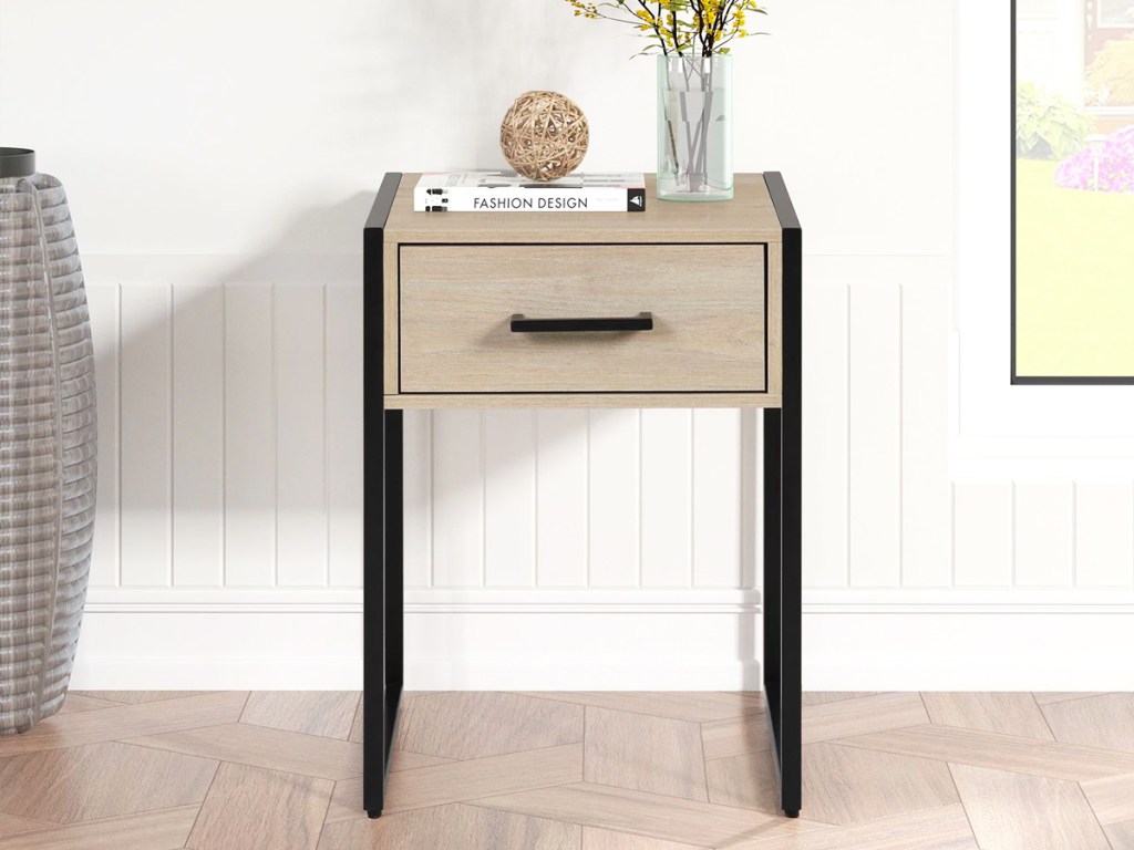 light wood and black nightstand with vase of flowers on top